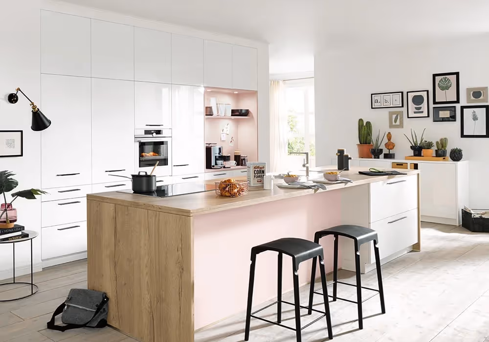 Modern kitchen with a wooden island, bar stools, and white cabinets. Decor includes plants and wall art.