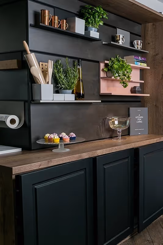 Kitchen shelves with plants, spice containers, cooking utensils, and colorful cupcakes on a wooden counter.