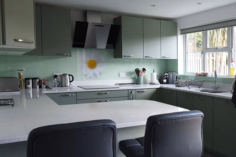 Modern kitchen with green cabinets, white countertops, and a flower design behind the stove.
