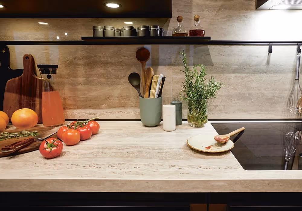 A kitchen counter with tomatoes, oranges, herbs, and utensils next to a stove.