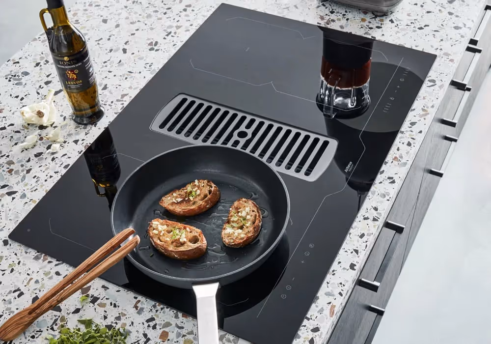 Three pieces of toast with toppings are cooking in a pan on a modern stovetop.