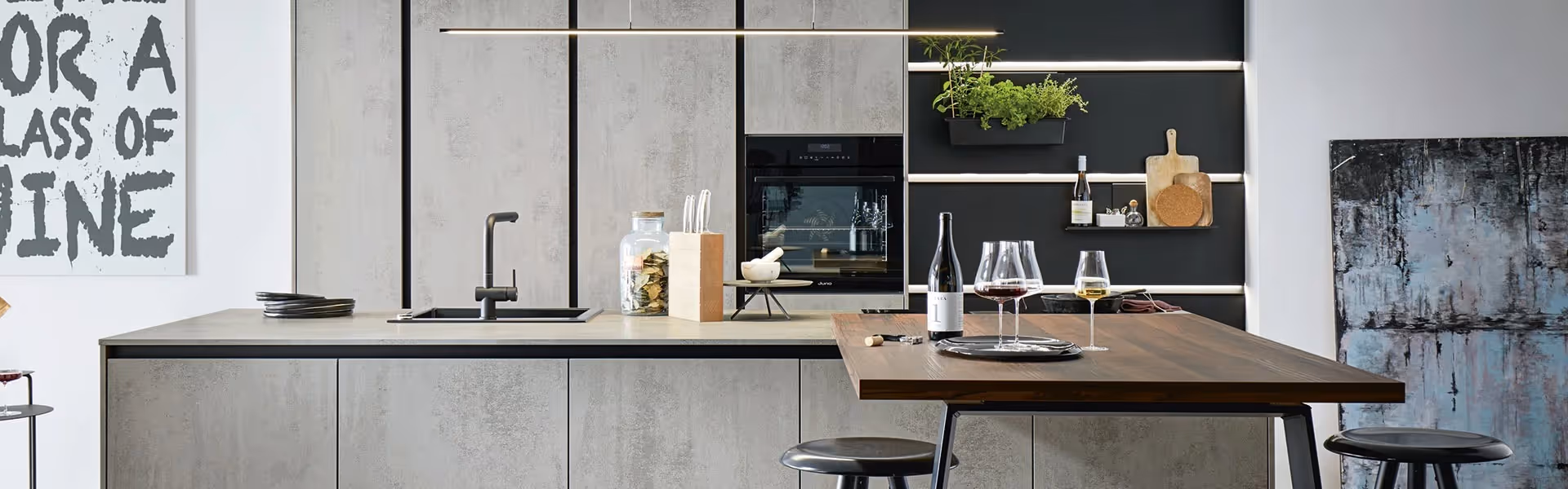 Modern kitchen with a wooden table set for two, featuring wine glasses and a bottle.