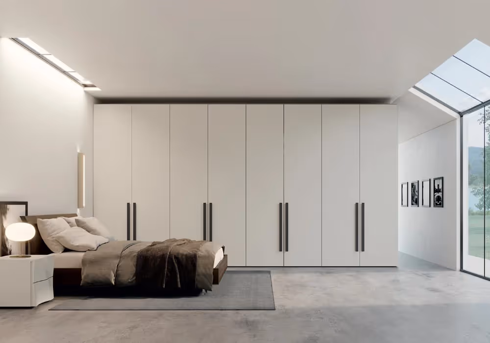 A modern bedroom with a large white wardrobe, double bed, nightstand, and lamp on the left side.