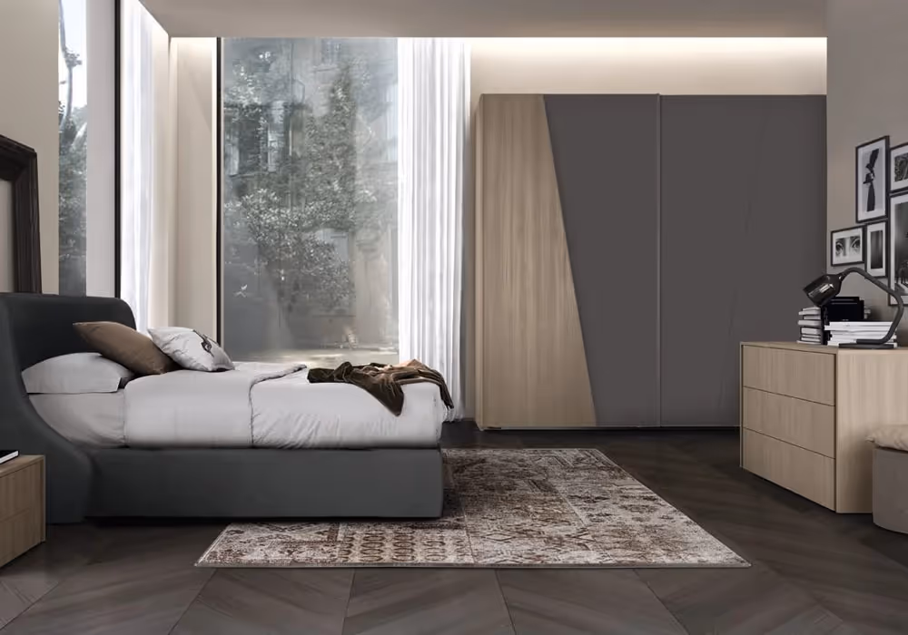 Bedroom with a large bed, wardrobe, dresser, and a bright window. Rug on dark wood floor.