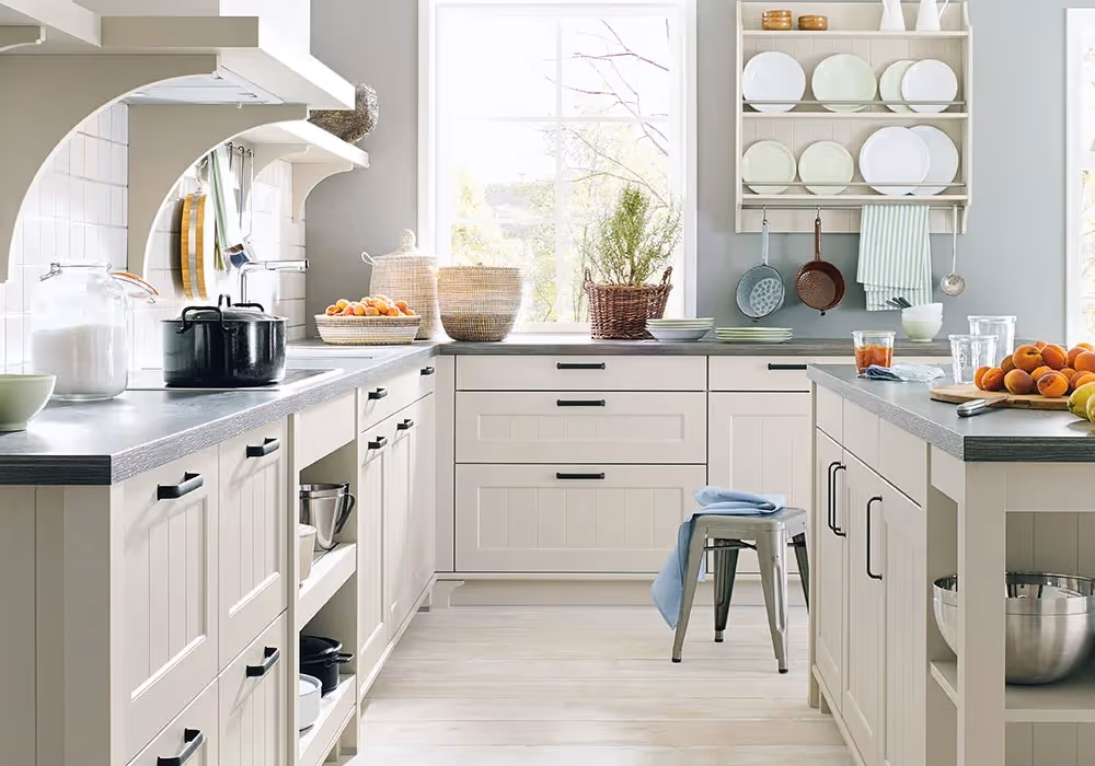 A bright kitchen with white cabinets, black countertop appliances, and shelves holding plates and glasses.