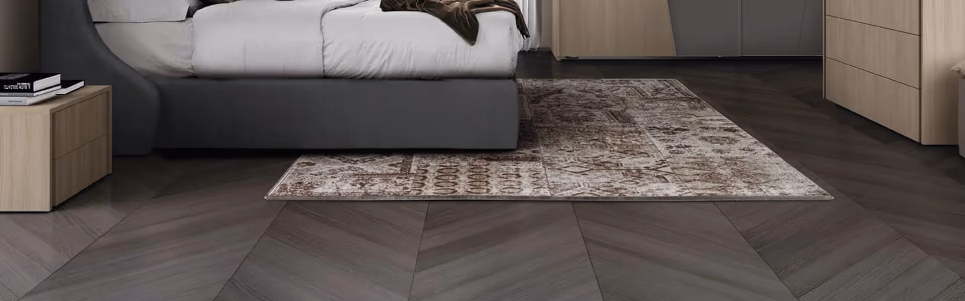 A bedroom with a gray bed and a patterned rug on a dark wooden floor.