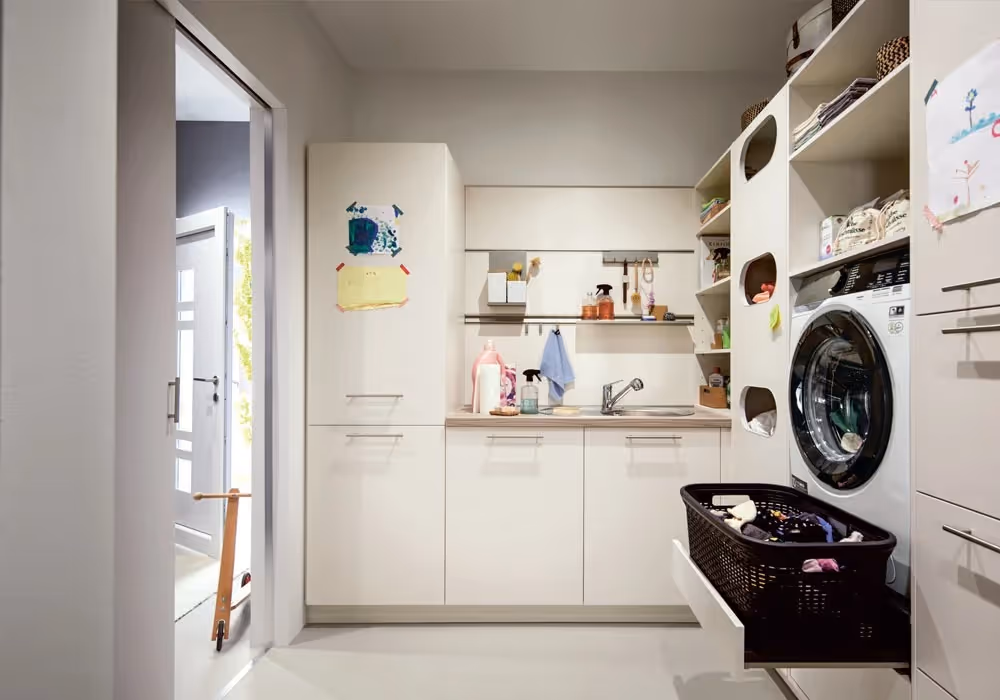 Laundry room with a washing machine, cabinets, and a basket of clothes on a pull-out shelf.