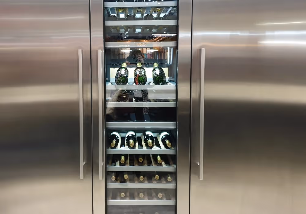 A stainless steel wine fridge with glass doors showing several bottles of wine inside.