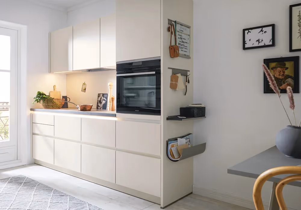 A modern kitchen features sleek white cabinets, an oven, and a wall display with utensils and photos.