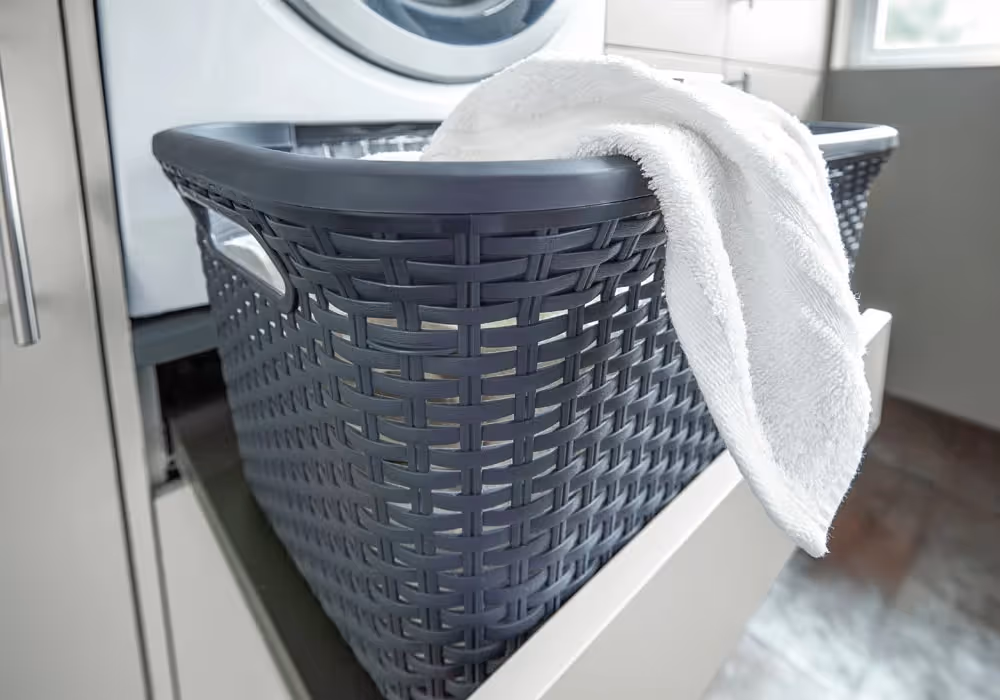 A white towel hangs over the edge of a black laundry basket in front of a washing machine.