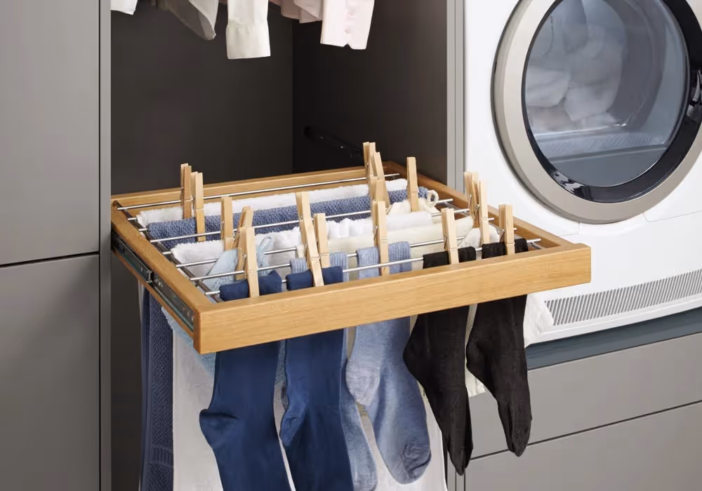 A pull-out drying rack with socks and clothes clipped on it near a washing machine.