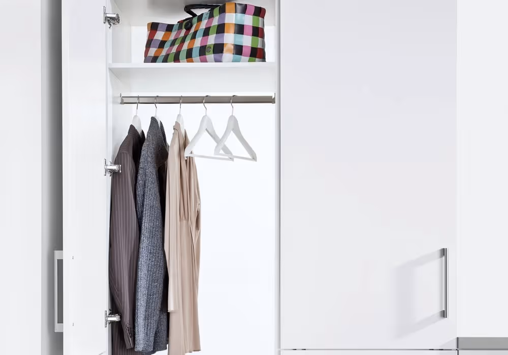 Open closet with three shirts hanging on hangers and a colorful bag on the top shelf.