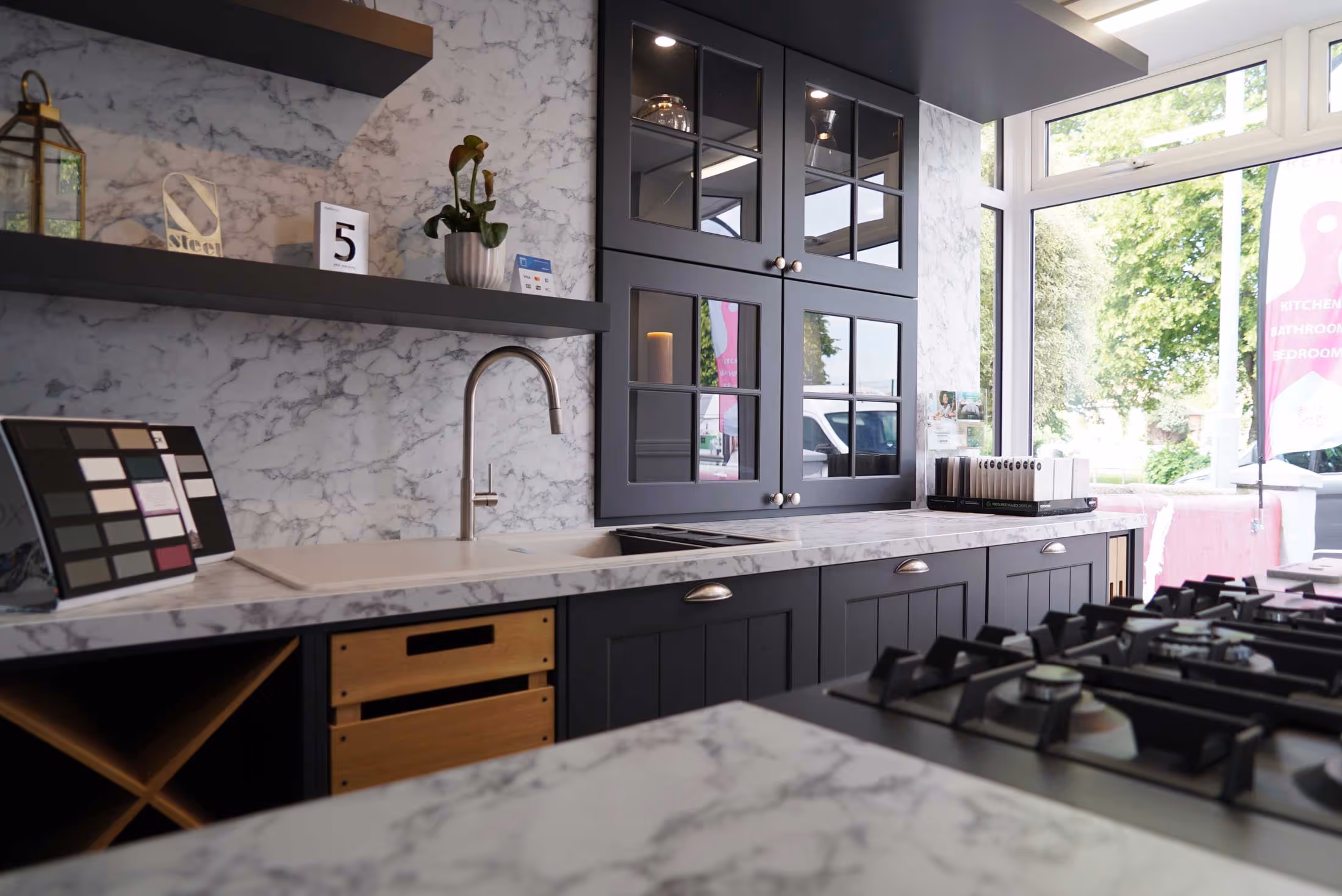 Modern kitchen with marble countertops, gas stove, sink, and dark cabinets with glass doors.