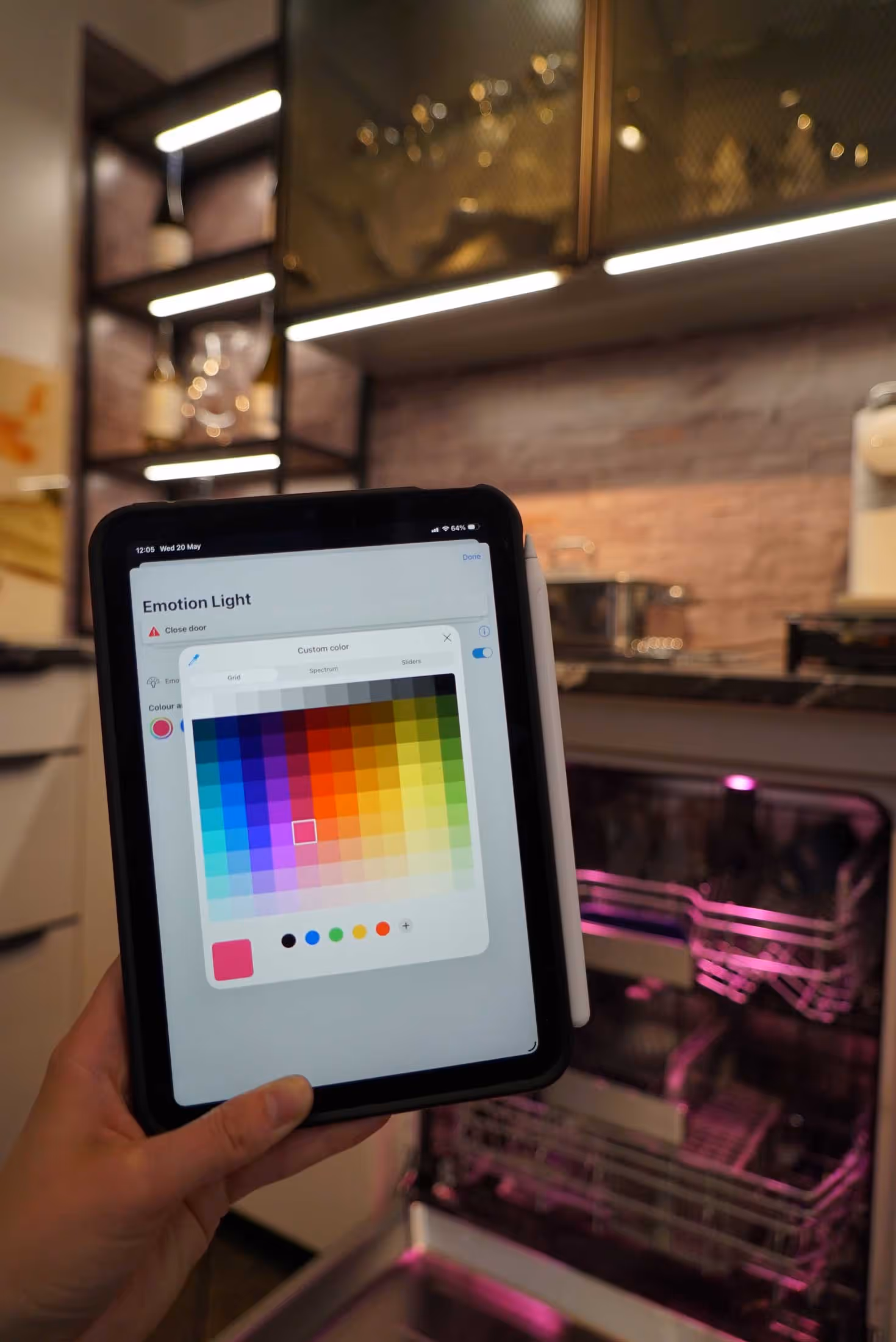 A person holds a tablet showing a color selection screen near an open dishwasher with pink lighting.