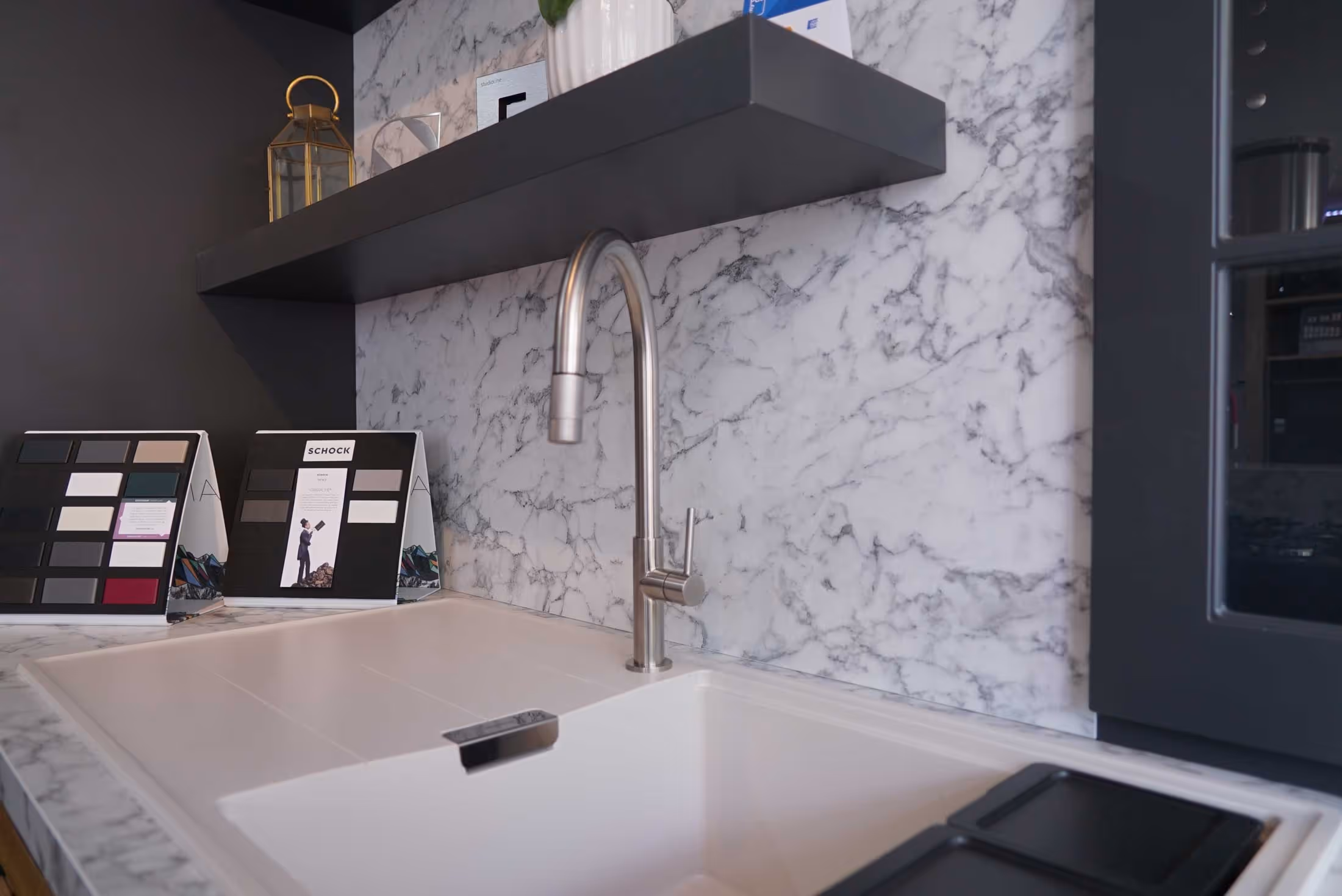 Modern kitchen sink with a tall faucet, set against a marble backsplash and a black shelf above.