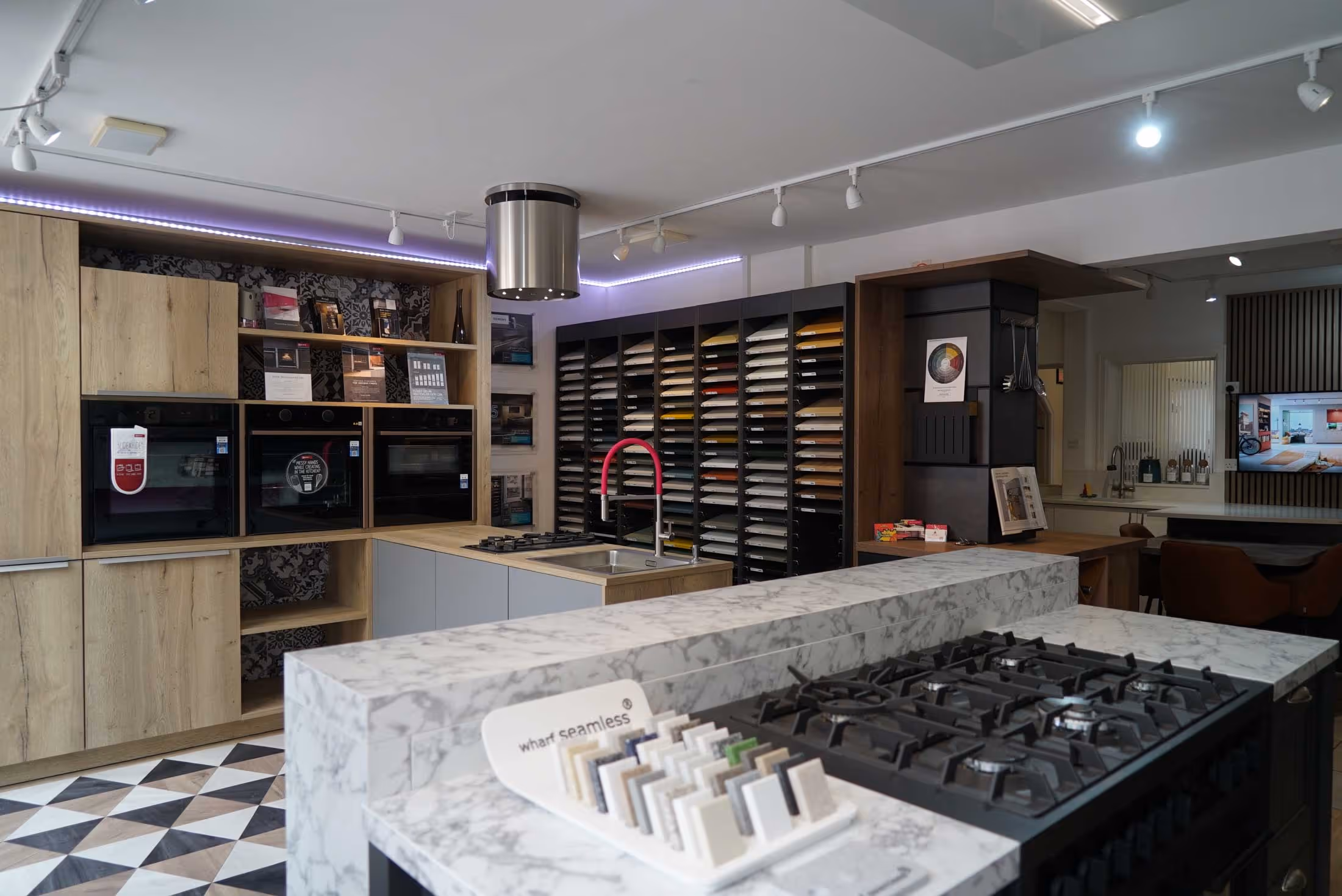 A modern kitchen showroom featuring various countertops, appliances, and a display of cabinet samples.