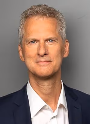 Middle-aged man with short gray hair wearing a dark blazer and white shirt, smiling slightly.