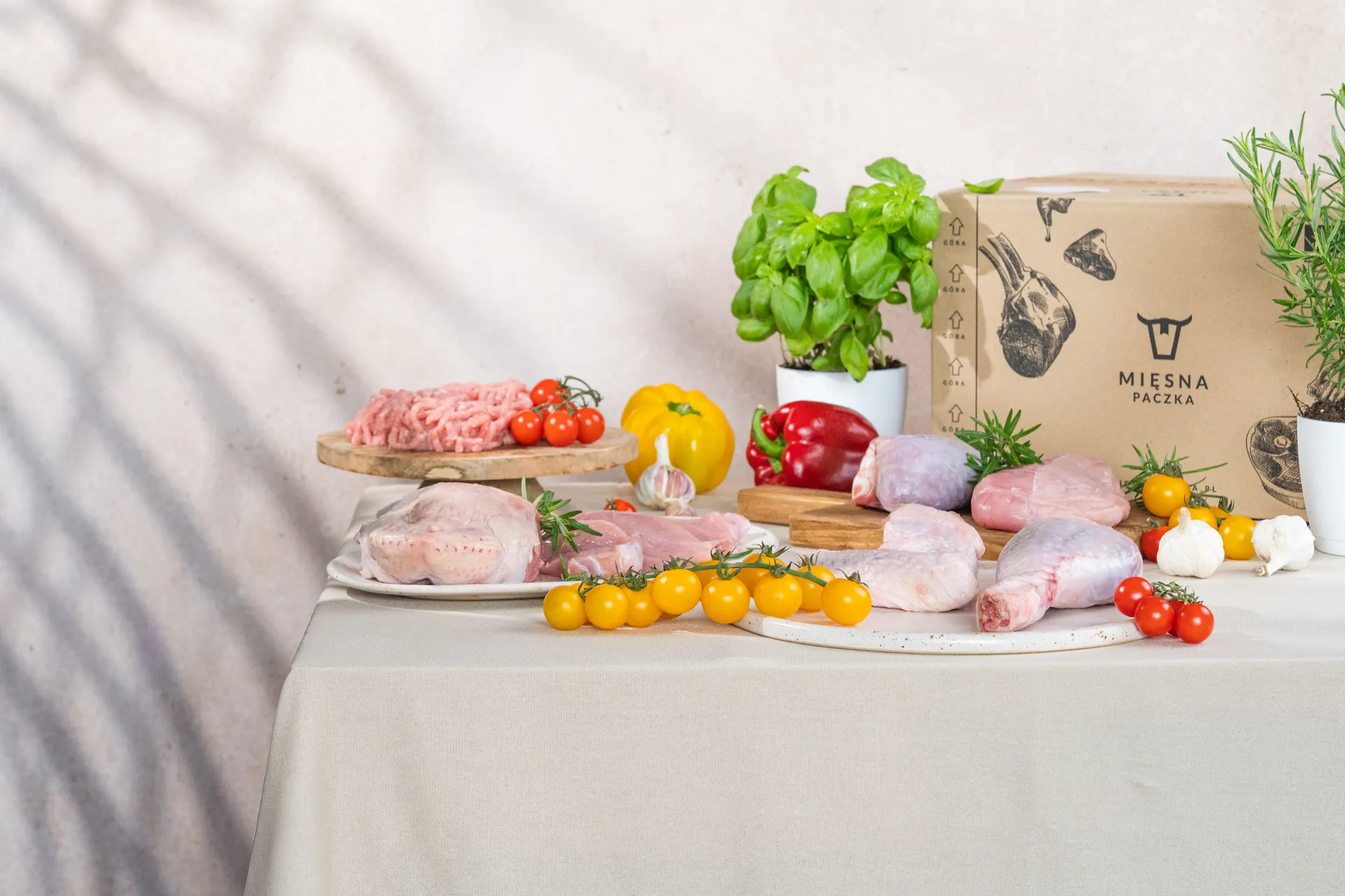 Surowe mięso z indyka – podudzia, skrzydła, filet i mielone – obok pudełka Mięsnej Paczki, z warzywami i ziołami