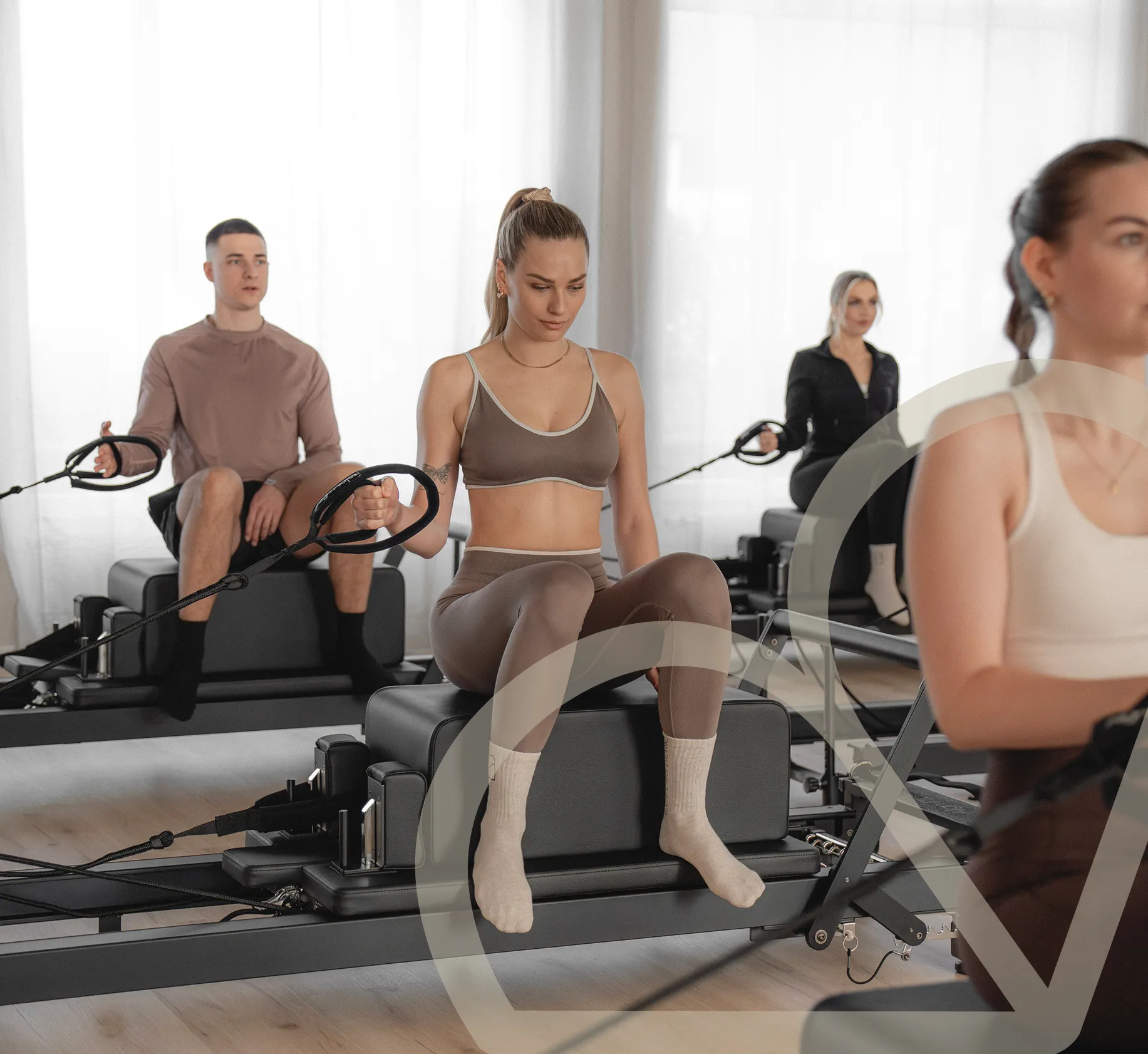 Mehrere Personen trainieren sitzend an Pilates-Reformern in einem hellen Pilatesstudio.