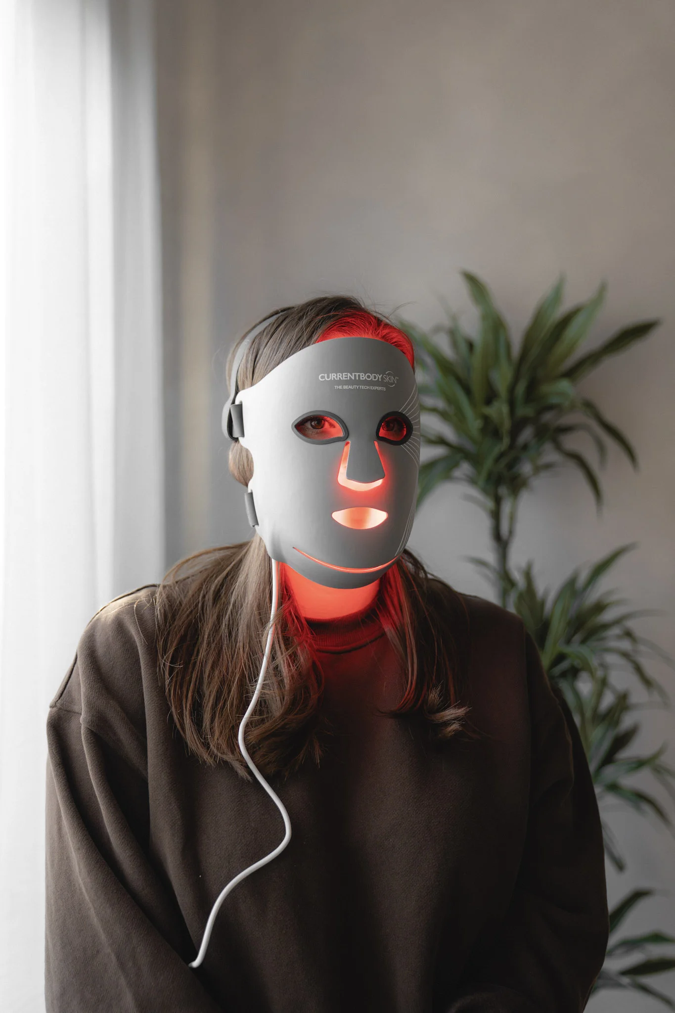 Person trägt eine LED-Lichttherapie-Maske mit roten Lichtern im Gesicht und am Hals.
