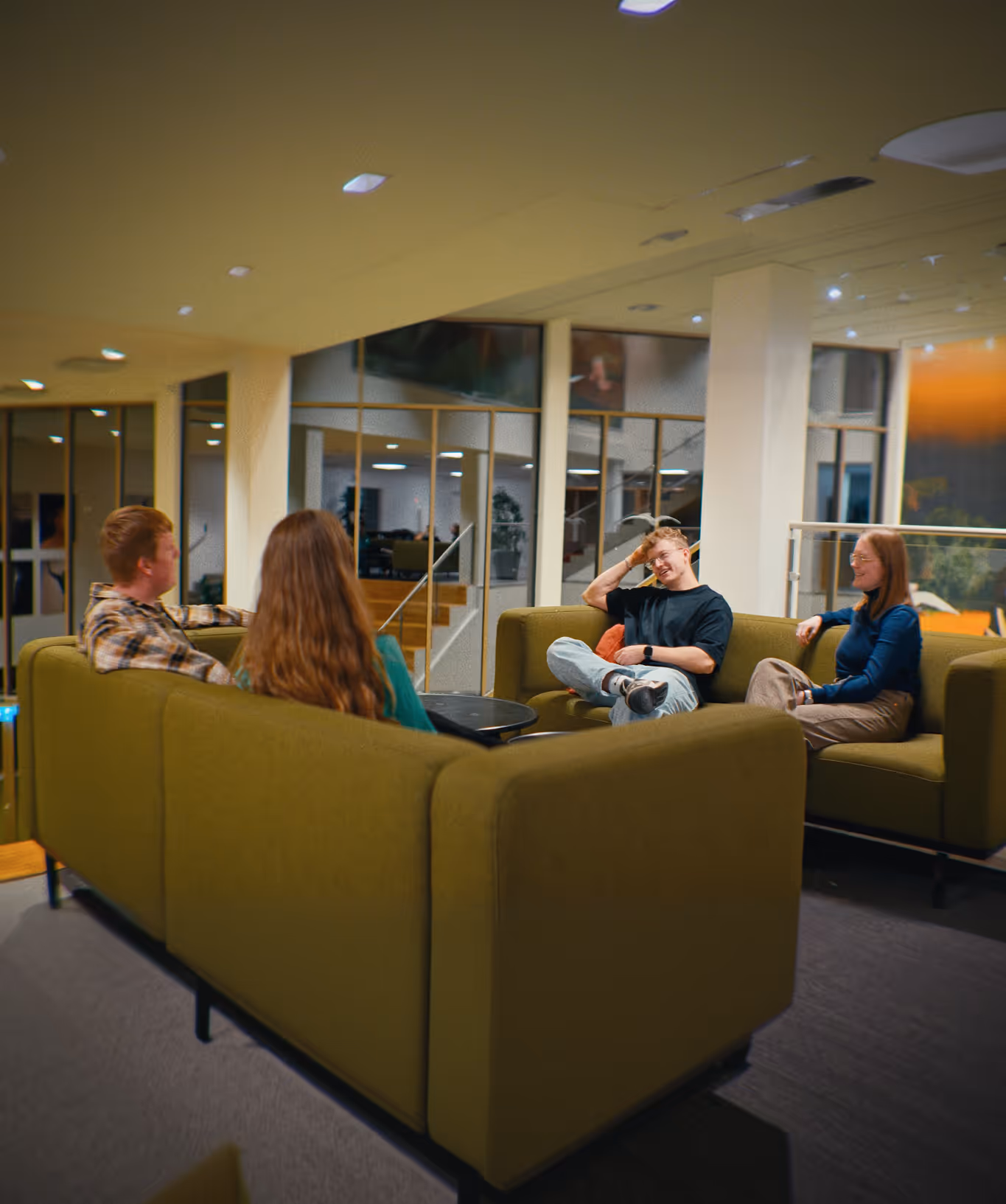 Fire unge sidder og taler i et moderne loungeområde med grønne sofaer.