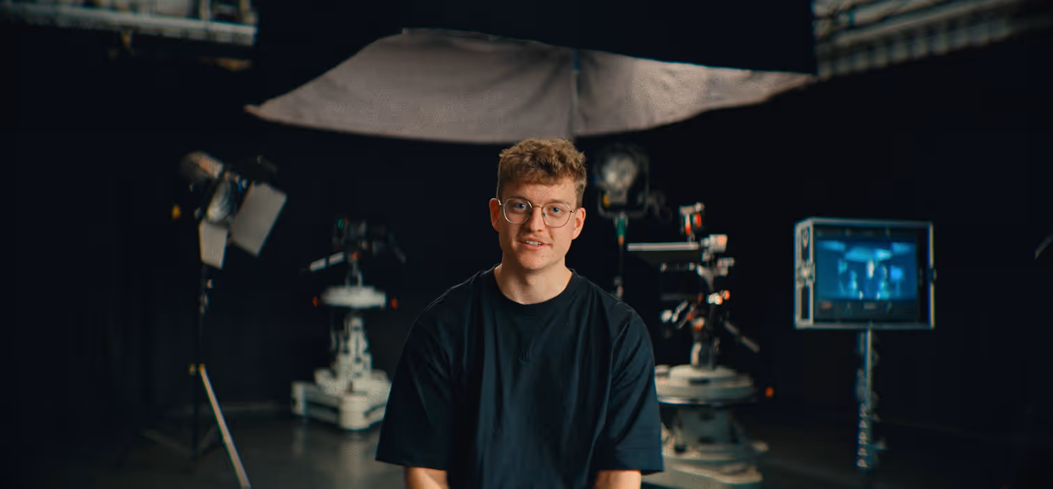 Ung mand med briller foran kameraudstyr og studiebelysning i et filmstudie.