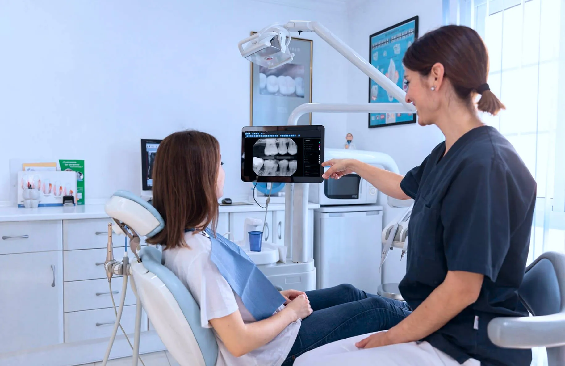 Dentist showing dental X-ray images on a screen to a woman sitting in a dental chair.