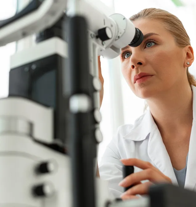 Female scientist or doctor closely examining a sample through a microscope in a laboratory.