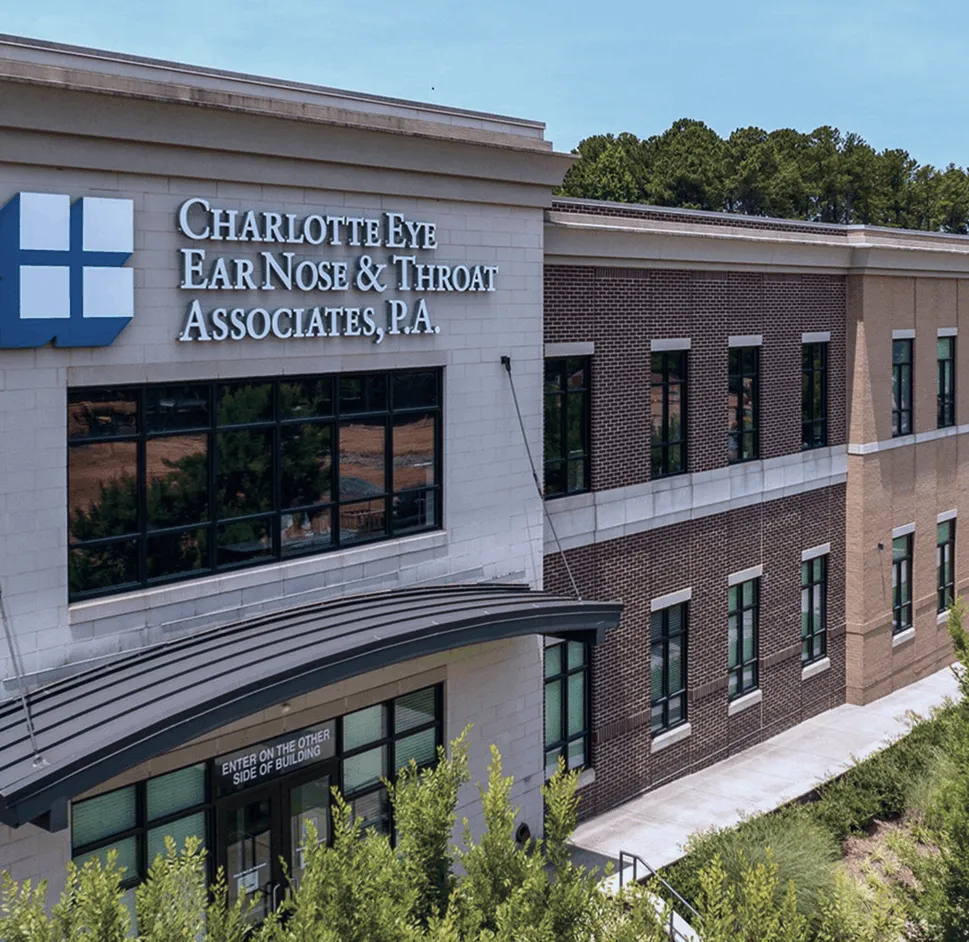 Exterior view of Charlotte Eye Ear Nose & Throat Associates medical office building with trees and bushes in the foreground.