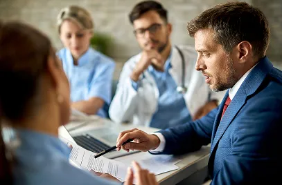 Group of medical professionals and a businessman discussing documents around a table in a meeting.