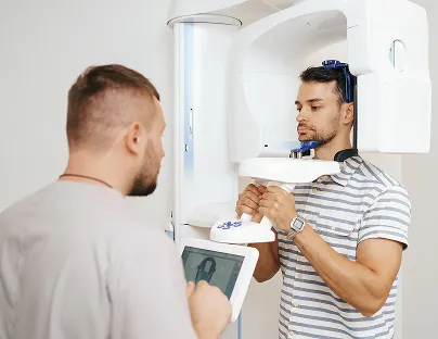 Man standing in a dental imaging machine while another man operates the control panel.