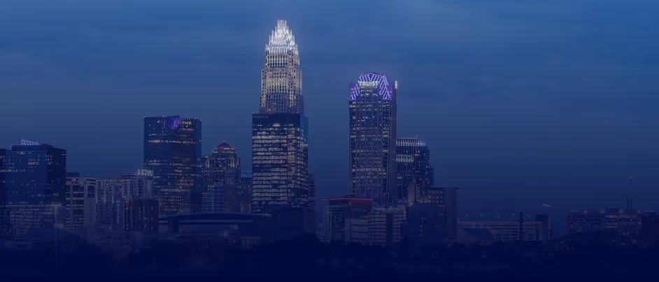 Nighttime city skyline with illuminated skyscrapers under a dark blue sky.