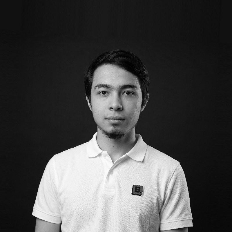 Portrait of a young man with short dark hair wearing a white polo shirt against a black background.