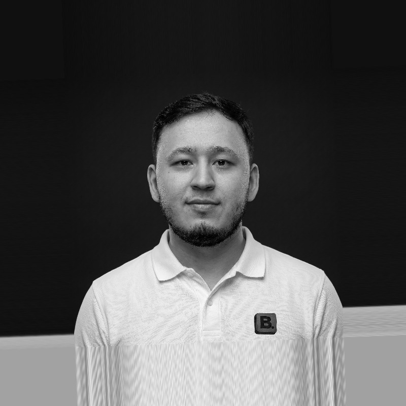 Man with short dark hair and beard wearing a white polo shirt against a black background.