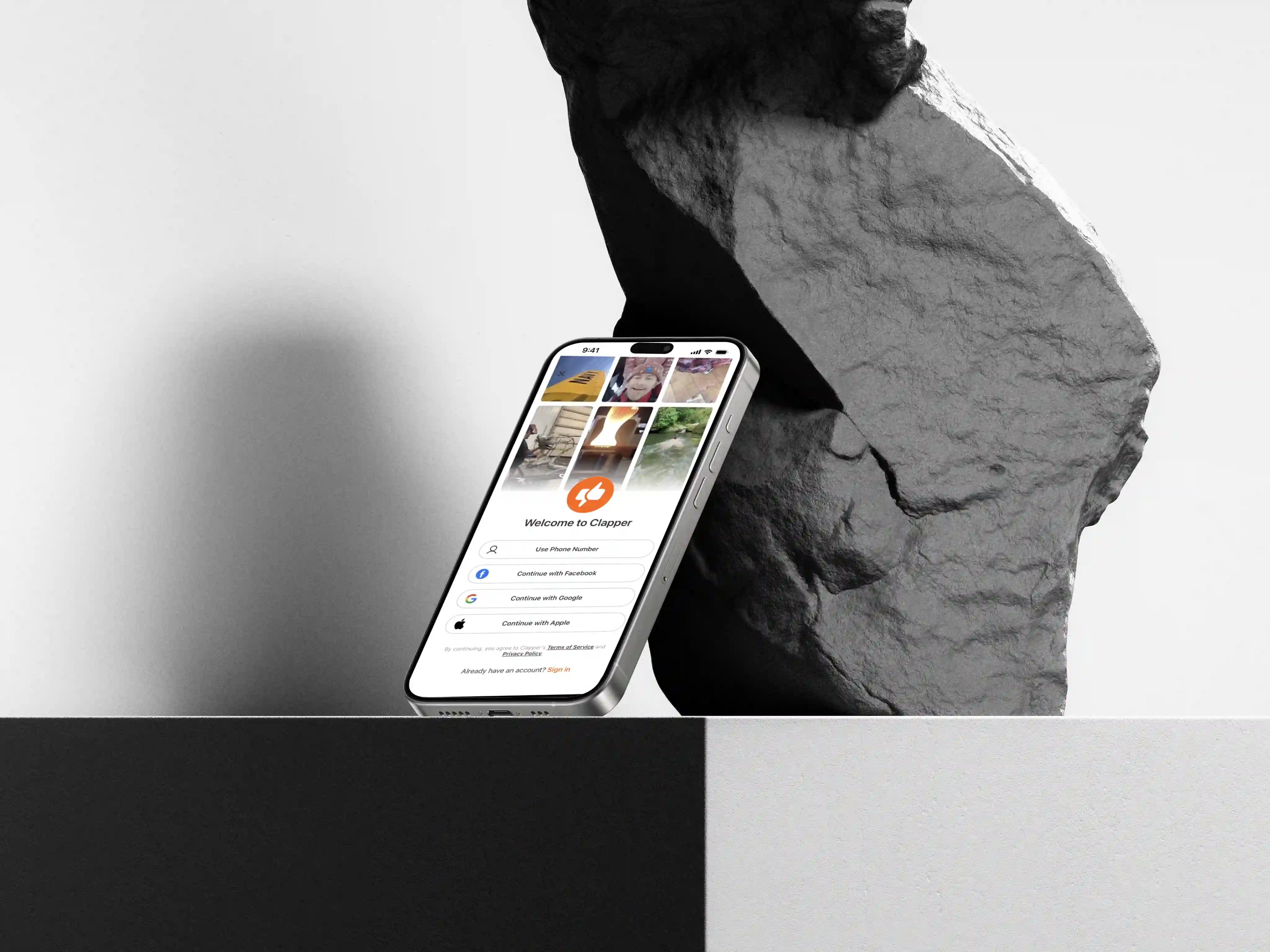 Smartphone displaying Clapper app login screen, leaning against a large textured rock.