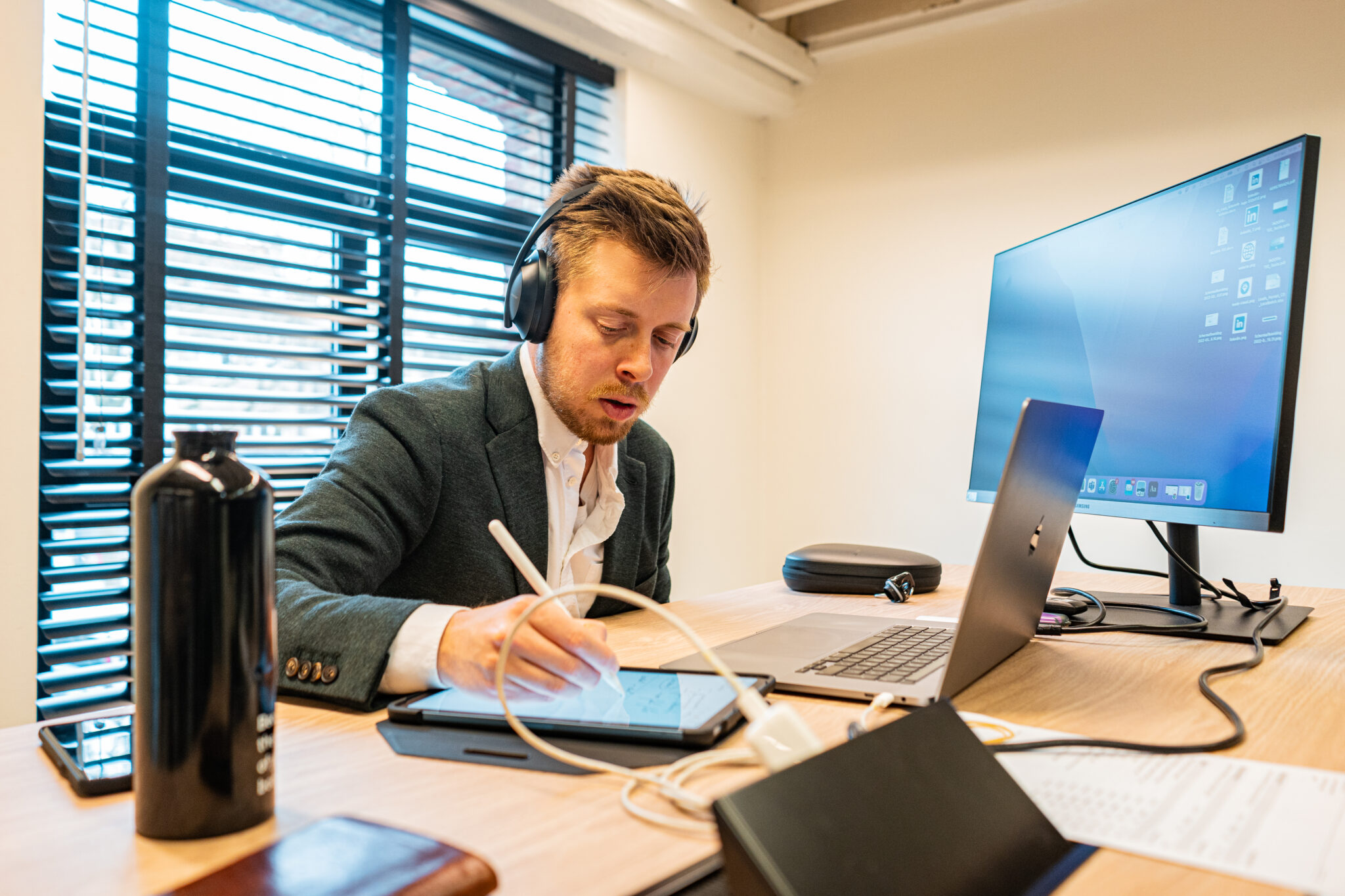 Medewerker werkt met koptelefoon aan een laptop en tablet in een kantooromgeving als beeld voor duurzaamheidsrapportage bij kmo’s.