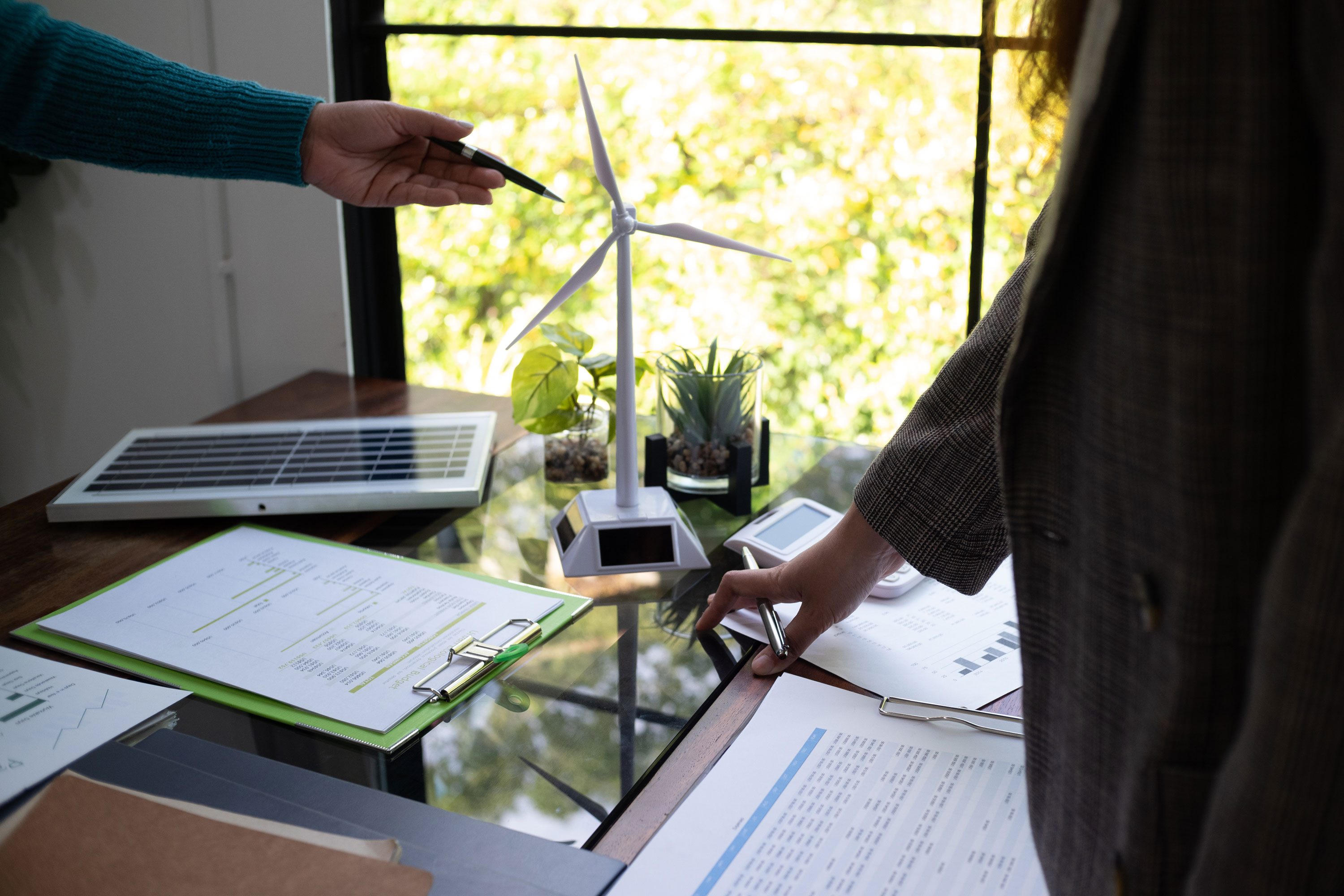 Twee medewerkers bespreken een windturbinemodel, zonnepaneel en bedrijfsdata als voorbereiding van een duurzaamheidsroadmap.