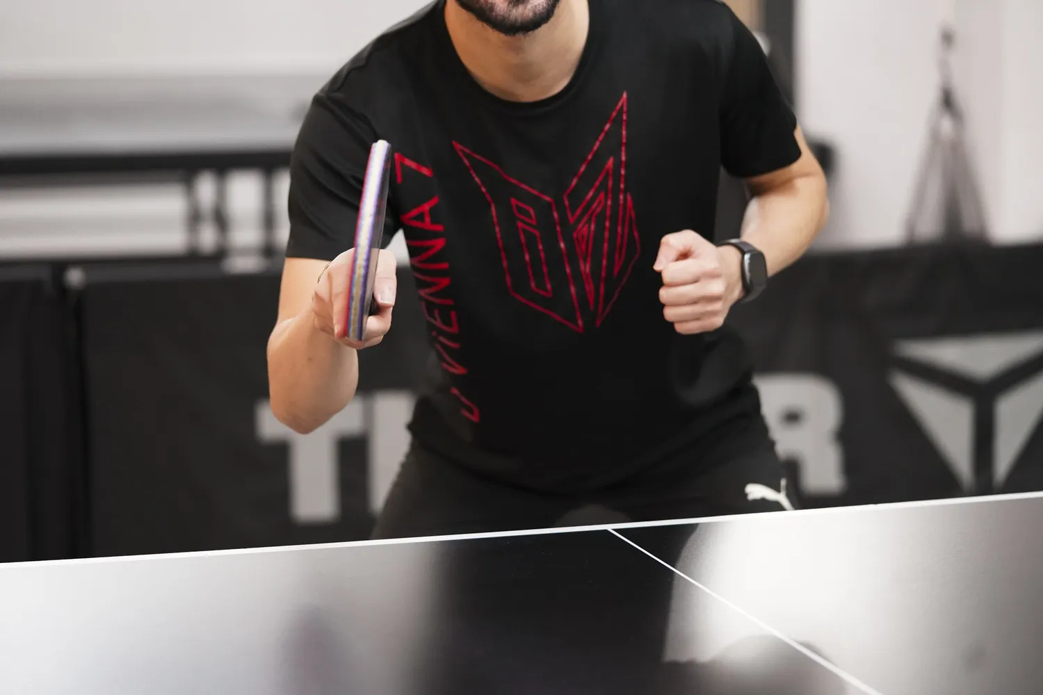 Mann spielt Tischtennis mit Schläger und Ball vor einem Tischtennistisch.