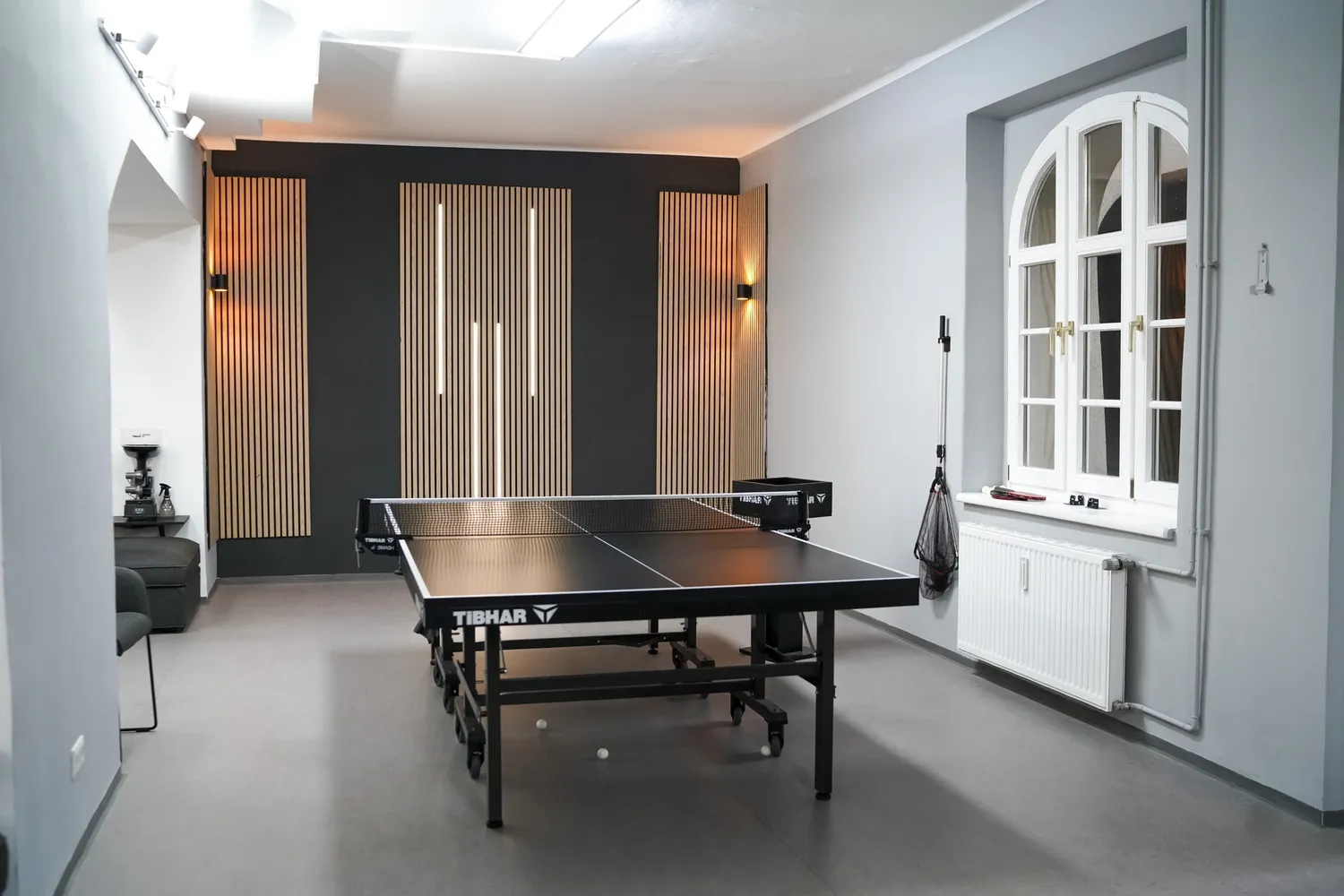 Moderner Raum mit schwarzem Tischtennistisch vor Wand mit Holzpaneelen und Fenstern.
