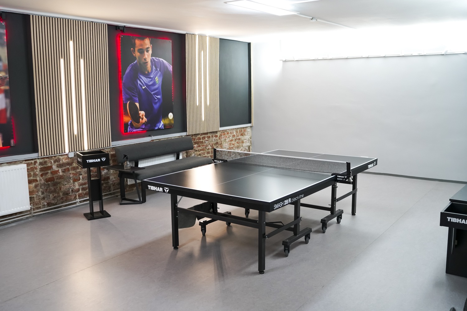 Moderner Tischtennisraum mit einem schwarzen Tischtennistisch und Sportlerfoto an der Wand.