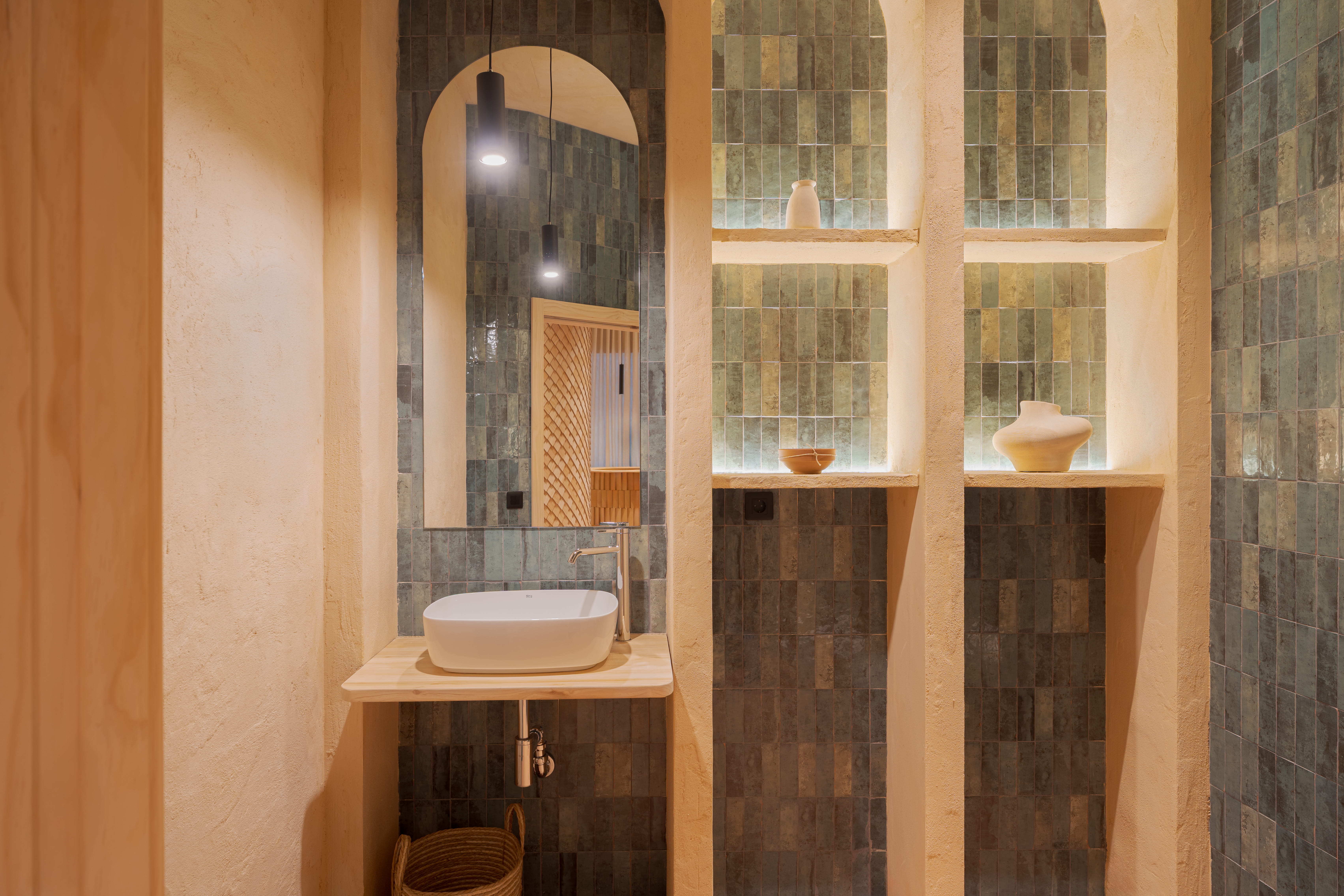 Lavabo moderno con espejo arqueado y estantes empotrados con jarrones decorativos.