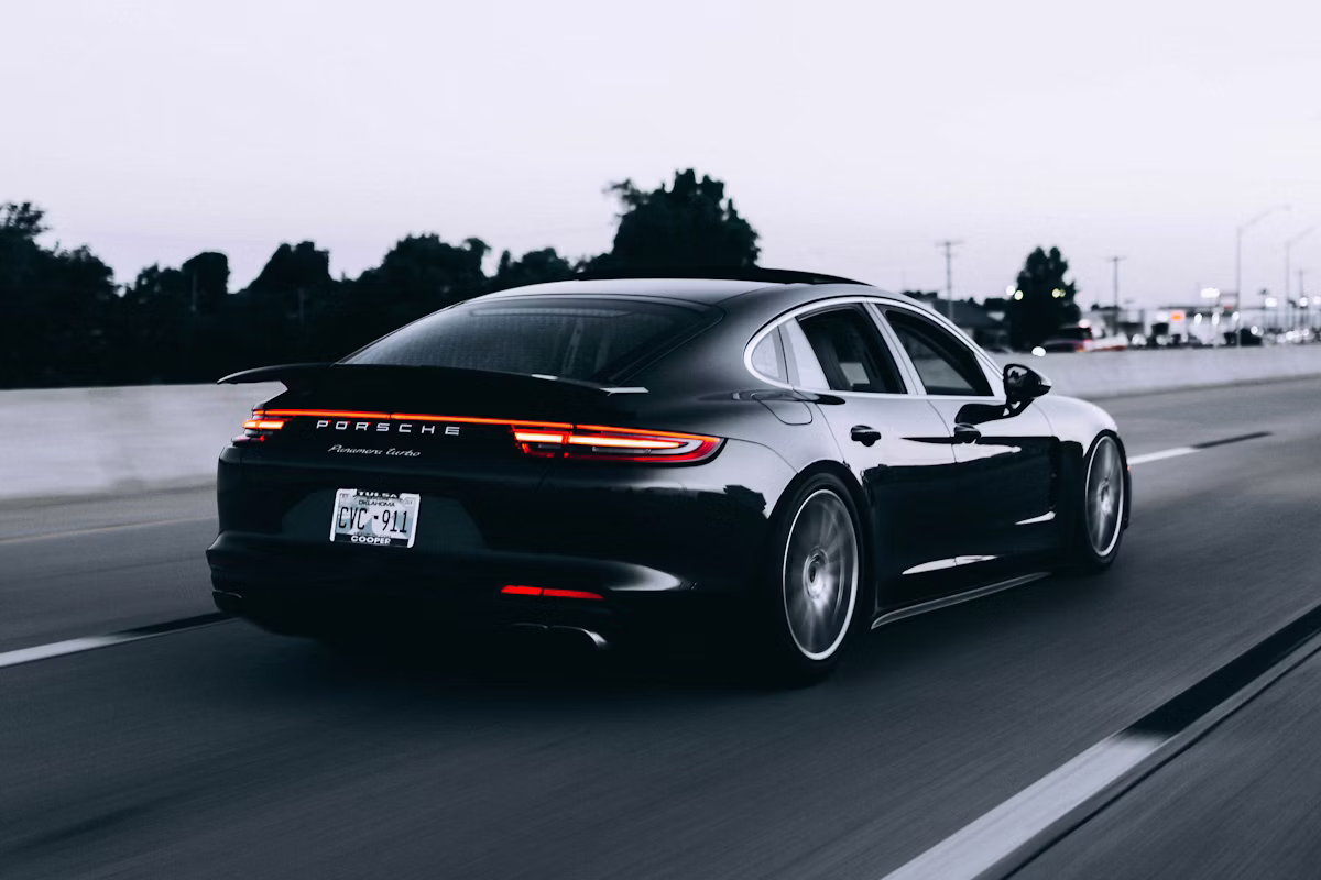 Black Porsche Panamera Turbo driving on a highway at dusk with rear lights on.