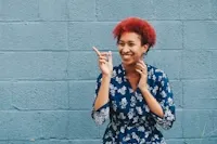Smiling person with red hair pointing to the left against a gray brick wall.