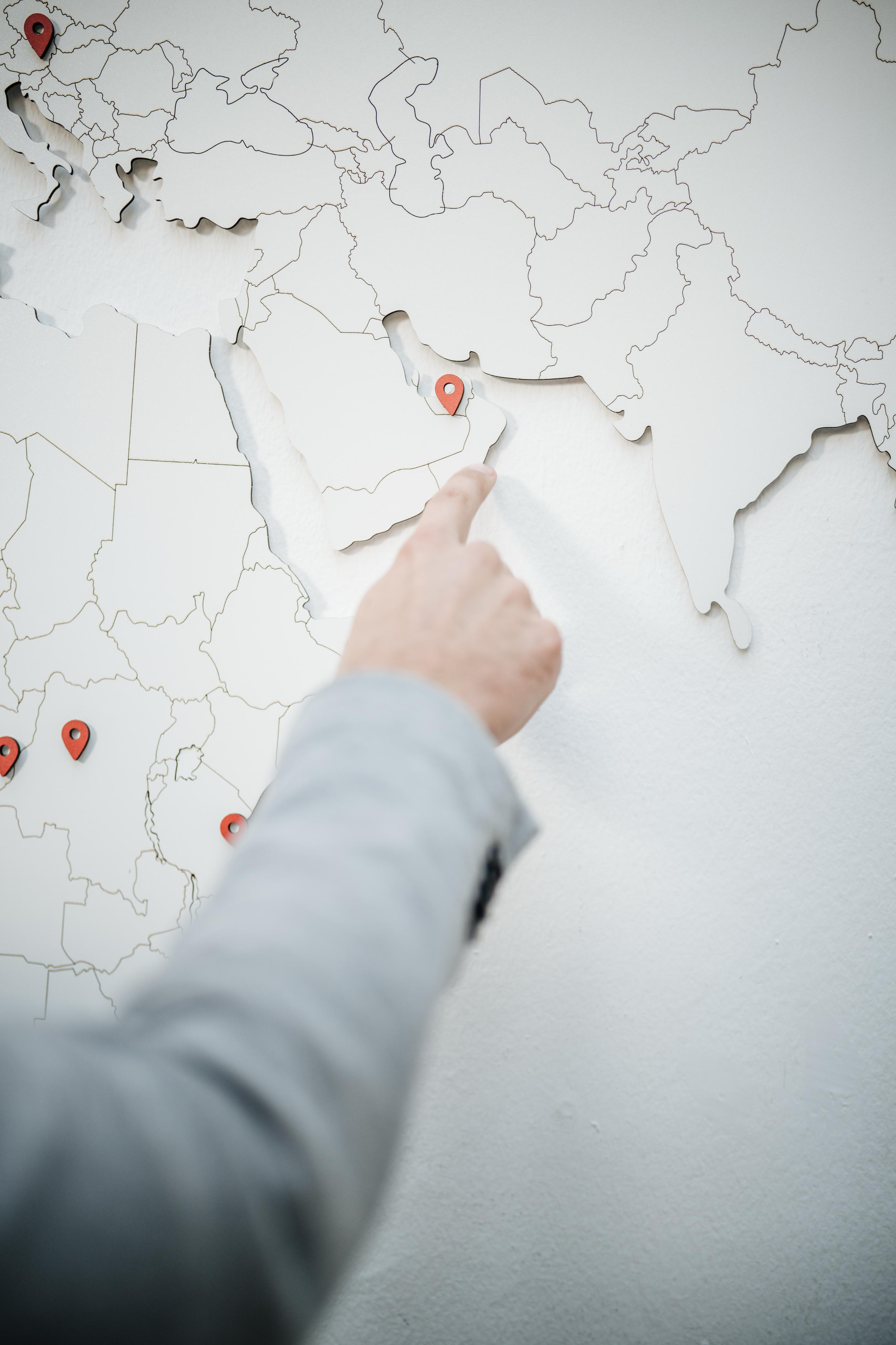 Person pointing to a location marker on a white map showing Asia and surrounding regions.