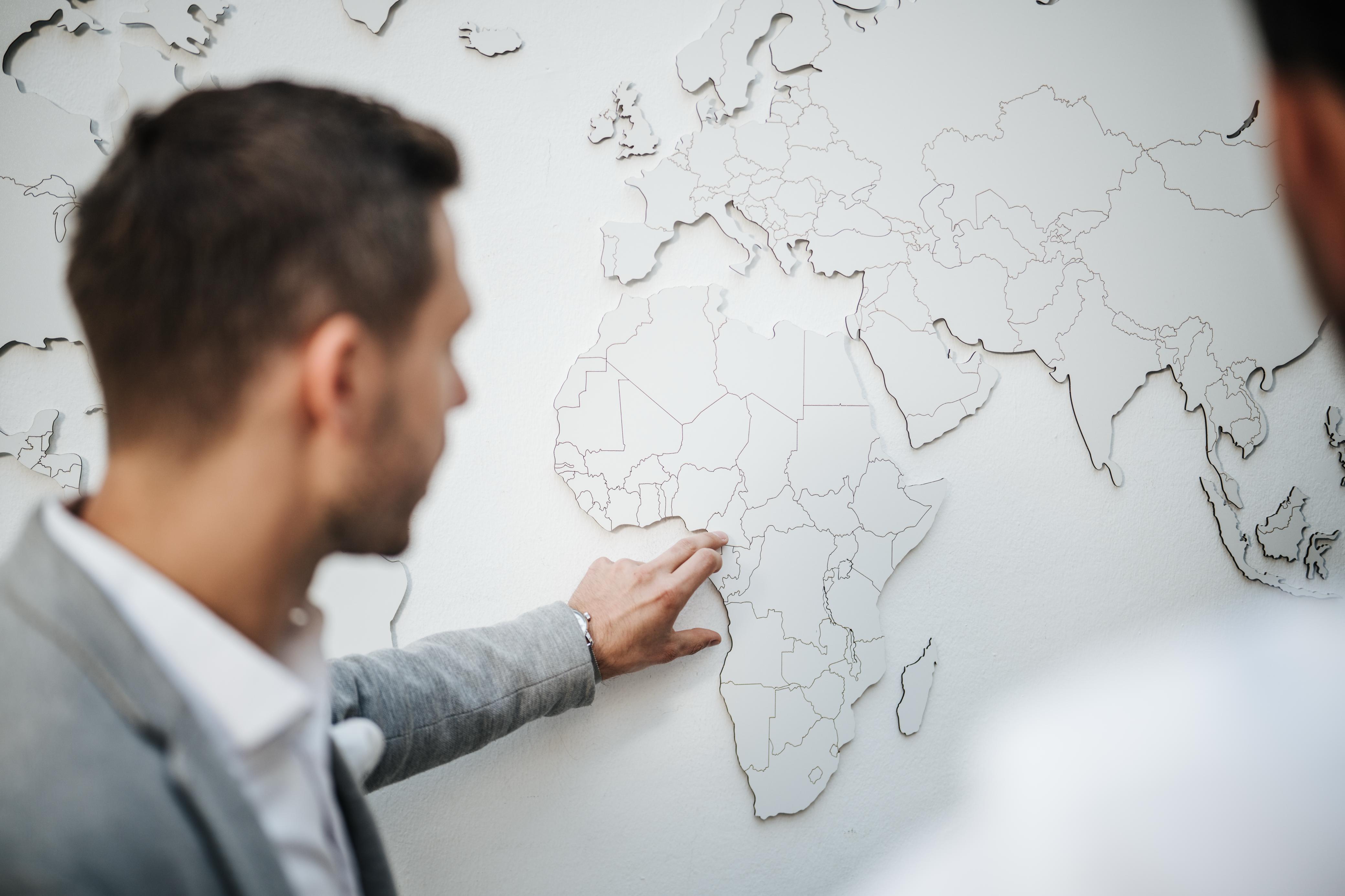 Man pointing at a white map of Africa with country borders on a white wall.