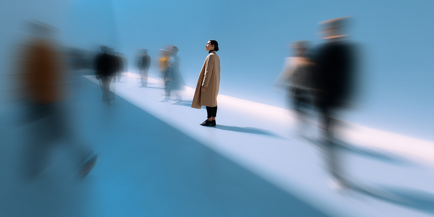 Person steht klar erkennbar auf einem hellen Lichtstreifen, während unscharf bewegte Personen vorbeiziehen – visuelle Metapher für Fokus und Wachstum in einer schnellen Marktdynamik