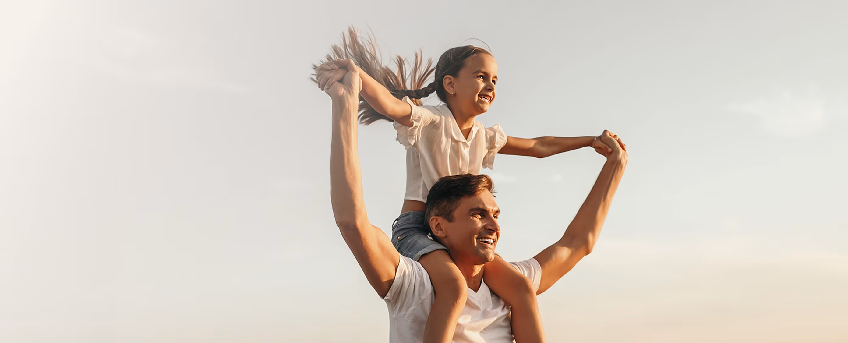 Padre sonriente cargando a su hija sobre los hombros al aire libre