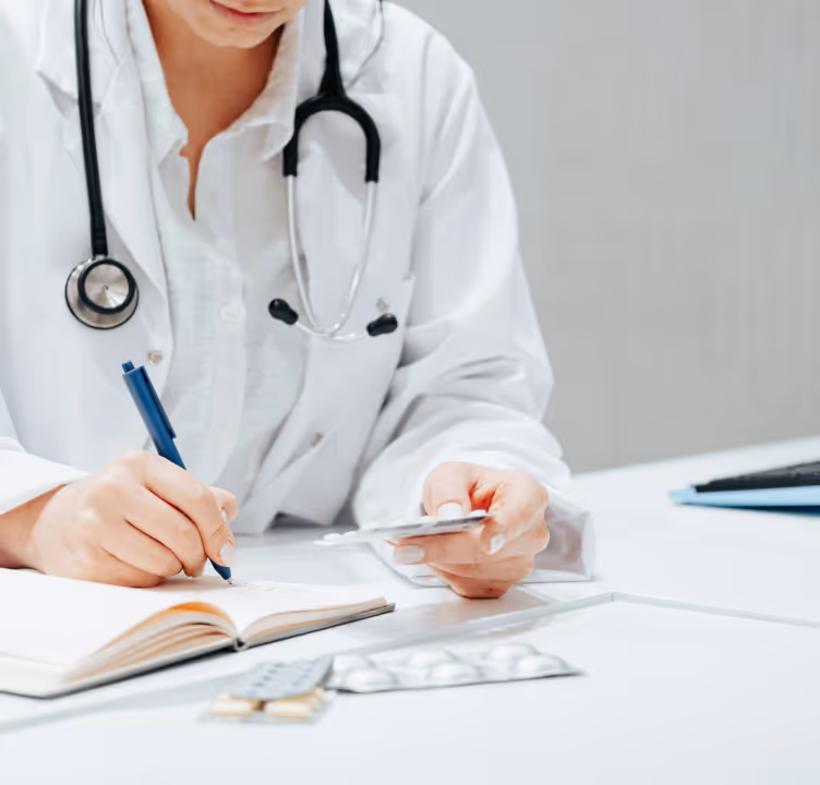 Médecin portant une blouse blanche avec un stéthoscope, écrivant une ordonnance tout en tenant des comprimés.