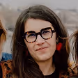 Femme portant des lunettes noires et un haut noir, souriant légèrement.