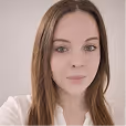 Portrait d'une femme aux cheveux longs et bruns, avec un maquillage léger et un haut blanc.
